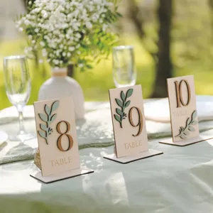 Numéros de table en bois avec feuilles vert sauge, panneaux rustiques pour déco de mariage.