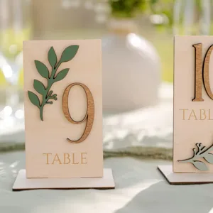 Détail de numéro de table en bois, feuille vert sauge, déco de table mariage moderne.