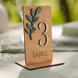 Panneau de numéro de table en bois vert sauge avec décor de feuilles pour mariage rustique.