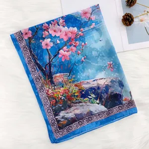 Close-up detail of blue silk scarf featuring pink cherry blossom print and geometric border.