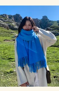 Close-up detail shot of a bright blue tassel wool scarf worn outdoors with natural scenery.
