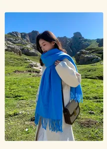 Outdoor detail view of a bright blue wool winter scarf with fringe worn by a model in nature.