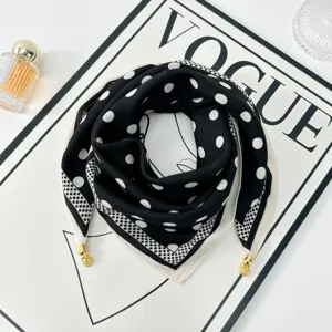 Black and white polka dot silk scarf with elegant gold corner charms, flat lay detail view.