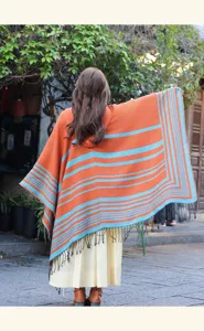 Vista de detalle exterior de un elegante poncho étnico de rayas naranjas y azules.