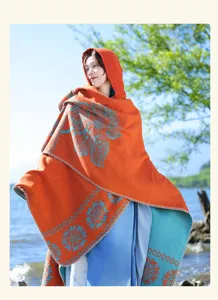 Outdoor detailed view of a warm ethnic style hooded shawl with floral pattern in orange.