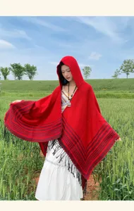 Plano detalle de un poncho capa rojo con capucha de estilo étnico con flecos en pradera verde.