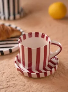 Vista detallada del juego de taza y platillo de café de cerámica a rayas rojas y blancas.