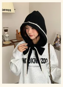 Black knitted balaclava hat for women with white trim and tie detail, cozy winter hood cap.