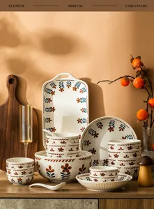 Detail of Japanese style ceramic tableware set with hand painted floral pattern on wooden table.