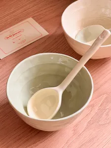 Close-up detail of glazed ceramic bowls and matching spoons on a warm wooden tabletop.