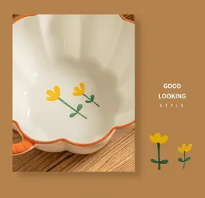 Ceramic noodle bowl detail showing cute yellow flower pattern and orange rim on wooden table.