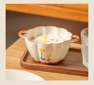 Detailed view of ceramic double-handle bowl with tulip pattern on wooden tray in home setup.