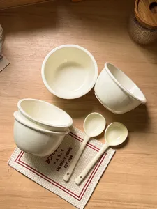 Detailed view of cream ceramic bowls and spoons on wooden table, ins style home tableware.