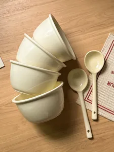 Detailed shot of Korean style ceramic bowls and spoons on a wooden table, elegant tableware.