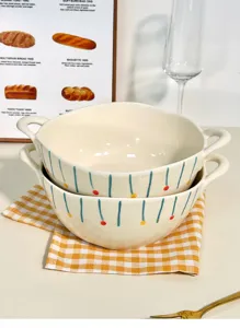 Ceramic double handled soup bowl detail showing cream color with painted stripes and colorful dots.