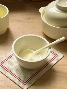 Cream yellow ceramic bowl and spoon set, tabletop detail view, minimalist homeware.