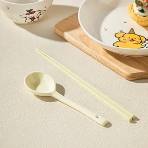Close-up detail of ceramic spoon and chopsticks with cute cartoon tableware set in kitchen.