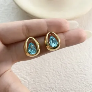 Nahaufnahme von Tropfen-Kristall-Ohrsteckern, Goldmetall und hellblauer Zirkonia.
