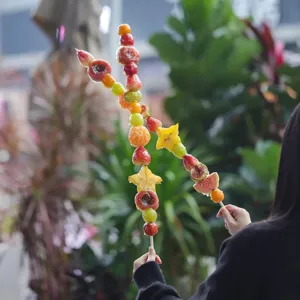 Close up detail view of extra long fruit tanghulu skewers held by hand outdoors.