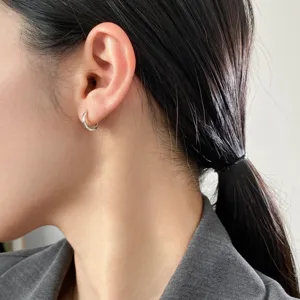 Nahaufnahme eines minimalistischen Silber-Creolen-Ohrrings am Ohr, glattes poliertes Design.