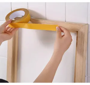Detailed view of yellow double-sided cloth tape being applied to a wooden frame surface.