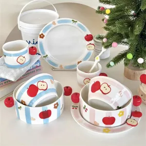 Detailed view of cute ceramic tableware set with stripes and red apple decorations.