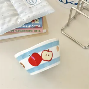 Detailed view of ceramic bowl with blue stripes and cute red apple pattern, tabletop decor.