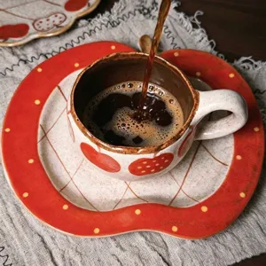 Close-up detail of retro ceramic coffee cup and saucer set with cute red apple pattern for home use.