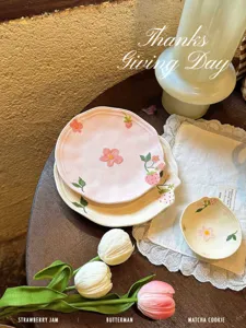 Primo piano di stoviglie in ceramica con eleganti piatti floreali rosa e fragole.
