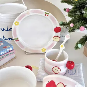 Detailed view of cute ceramic tableware set with pink stripes, apple and flower designs.