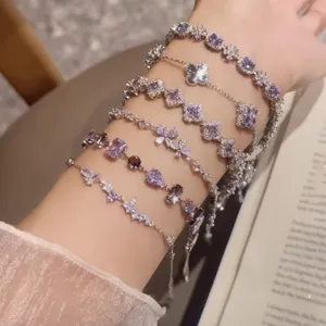 Vista detallada de pulseras de plata apiladas con cristales morados y tréboles en la muñeca.