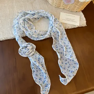 Gedetailleerd overzicht van witte chiffon halsdoek met blauwe bloemen en chique knoop.