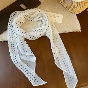 Detail shot of a white chiffon scarf with black polka dots, elegant French style accessory.