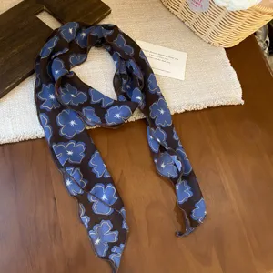 Close-up view of a chic chiffon floral scarf featuring blue blossoms and dark brown fabric.