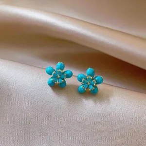 Close-up detail shot of exquisite blue floral stud earrings with gold stamen accents, elegant.