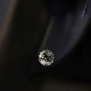 Close-up detail shot of a sparkling round-cut zircon ear stud with brilliant fire and prong setting.