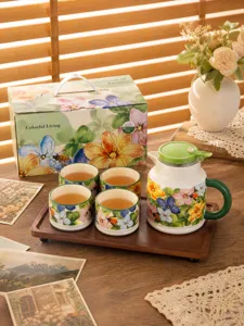 Exquisite ceramic tea set detail with floral teapot, cups, and wooden tray on table.