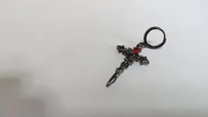 Dettaglio orecchino a croce gotica scura, con texture metallica e gemma rossa per donna.