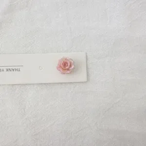 Exquisite pink rose stud earring detail on white card, sweet minimalist floral jewelry design.