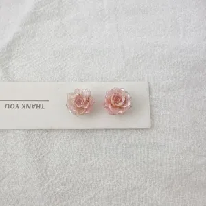 Close-up detail of sweet pink rose resin stud earrings with card, minimalist jewelry design.
