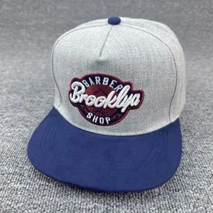 Gorra snapback gris con ala plana azul y parche bordado elegante en la parte delantera.