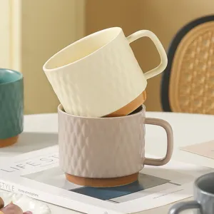 Detailed shot of stacked ceramic mugs with textured diamond pattern on white tabletop.