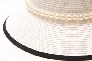 Gros plan détail d'un chapeau de paille blanc avec perles et élégante bordure noire.