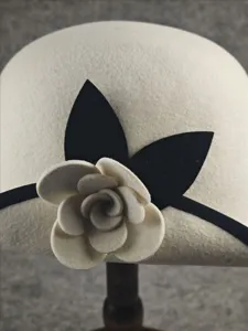 Close-up detail of beige wool bucket hat featuring black ribbon and felt camellia flower.