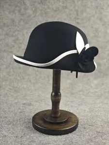 Close-up detail of a black wool felt cloche hat with white trim and camellia flower.