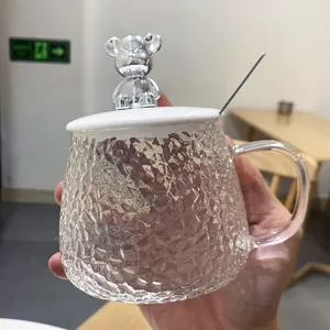 Close up detail of clear textured glass coffee mug with cute silver bear lid and spoon.