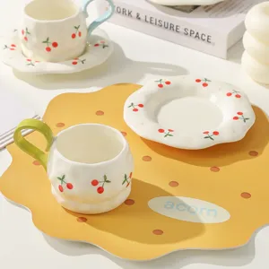 Handmade ceramic coffee cup and saucer set with cute cherry pattern for home office desk decor.