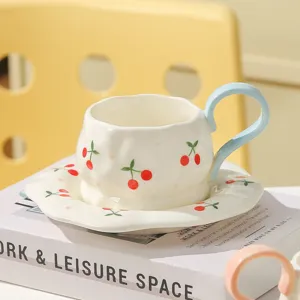 Ceramic coffee cup and saucer set with cute red cherry pattern and blue handle for afternoon tea.