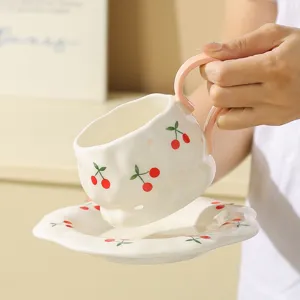 Hand-molded ceramic coffee cup and saucer set with cute red cherry pattern and pink handle.