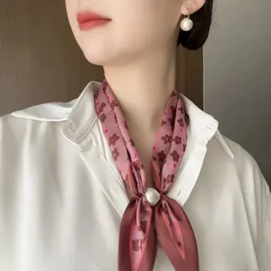 Detail view of a vintage floral silk scarf with pearl magnetic buckle worn on white shirt.